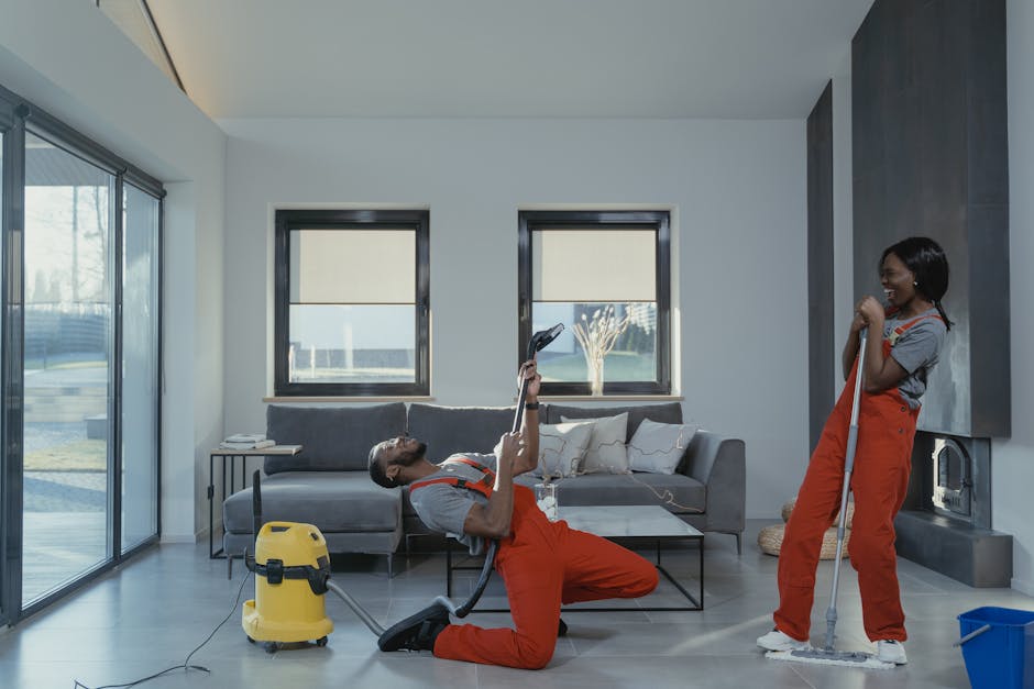 A professional cleaner with dark hair tied back, dressed in a black uniform, performing surface cleaning in a tidy home environment. She is using a yellow cloth to wipe a wooden table surface that hol